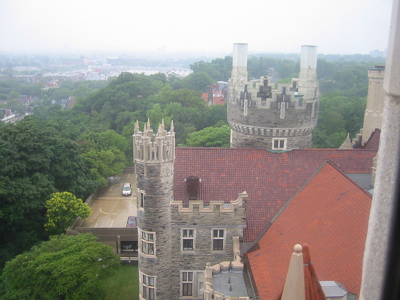 View of Casa Loma from one of its towers showing the main roof and two towers and part of the parking lot with parts of the city below in the background